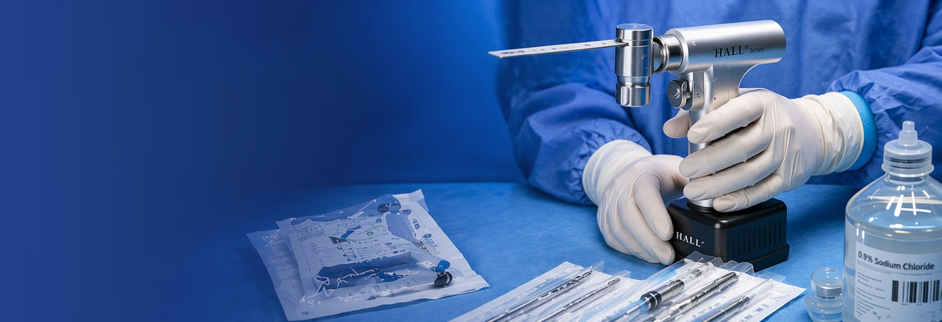 Gloved surgical professional holding a HALL Series surgical power tool with surgical instruments and a 0.9% Sodium Chloride IV bottle on a blue surgical drape
